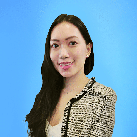 Woman with long black hair and a patterned jacket smiling in front of a plain blue background.