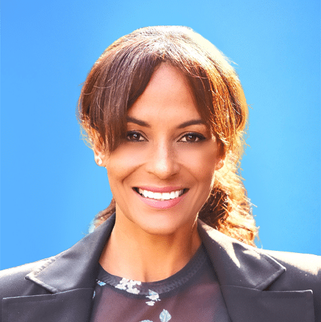 Woman with brown hair wearing a black blazer smiles in front of a bright blue background.
